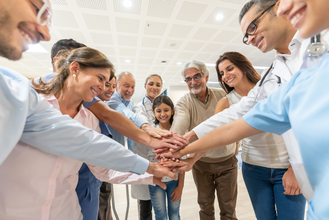 Group of healthcare workers and patients of different ages in a huddle all with hands in smiling